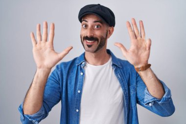 Sakallı İspanyol bir adam tecrit edilmiş arka planda durup dokuz numaralı parmaklarıyla işaret ederken kendinden emin ve mutlu gülümsüyor.. 