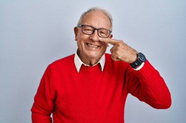 İzole edilmiş arka planda duran gri saçlı yaşlı bir adam,... el parmağı ve burunla işaret ediyor, neşeli bir şekilde gülümsüyor. güzellik konsepti 