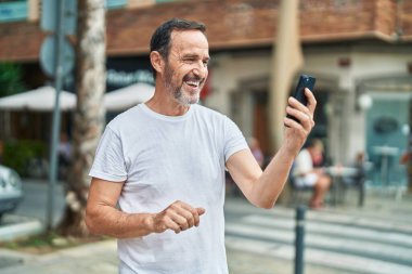 Orta yaşlı bir adam sokakta video araması yaptığından emin gülümsüyor.
