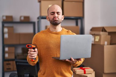 Sakallı genç ve kel bir adam. Küçük bir iş yerinde çalışıyor. Dizüstü bilgisayarıyla kameraya bakıyor. aşk ifadesi. 