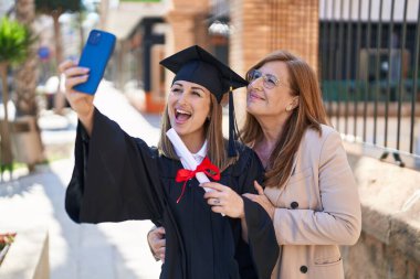 Mother and daughter making selfie by the smartphone celebrating graduation at university