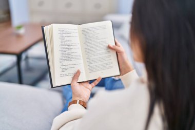 Evdeki kanepede oturmuş kitap okuyan genç İspanyol kadın.