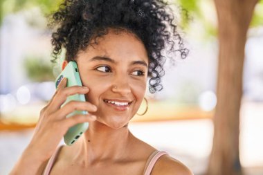 Genç İspanyol kadın gülümsüyor. Parktaki akıllı telefondan konuşuyor.