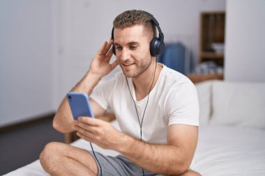 Young caucasian man listening to music sititng on bed at bedroom