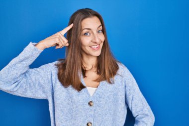 Young woman standing over blue background smiling pointing to head with one finger, great idea or thought, good memory 