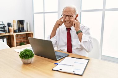 Ofiste çalışan kıdemli bir adam yüksek sesli müzik sesi için bilgisayarla kulaklarını parmaklarıyla kapatıyor. sağır kavramı. 