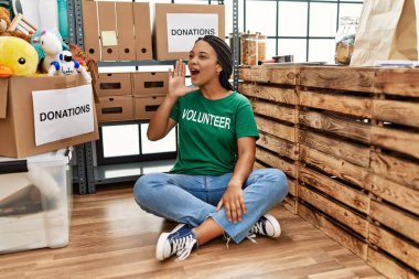 Young african american woman wearing volunteer t shirt at donations stand shouting and screaming loud to side with hand on mouth. communication concept. 