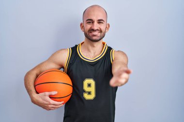 Sakallı, basketbol forması giyen, elinde top tutan, dostça el sıkışan genç ve kel bir adam. başarılı iş. 