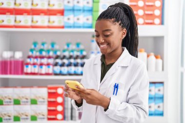 Eczanede çalışan akıllı telefonu kullanan Afrikalı Amerikalı kadın eczacı.