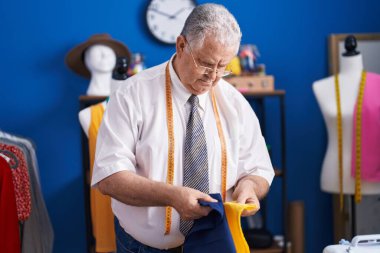 Orta yaşlı, gri saçlı bir adam terzi dükkanında elbise tutuyor.