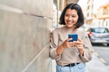 Sokakta akıllı telefon kullanan kendine güvenen genç bir kadın.