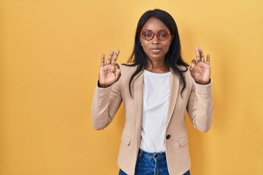 African young woman wearing glasses relax and smiling with eyes closed doing meditation gesture with fingers. yoga concept. 