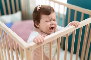 Adorable toddler standing on cradle crying at bedroom