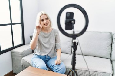 Kafkasyalı genç bir kadın evinde akıllı telefonuyla video kaydı yapıyor. Bir numarayı gösterip işaret ederken kendine güvenen ve mutlu bir şekilde gülümsüyor.. 