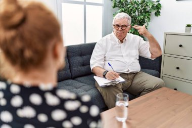 Konsültasyon ofisinde kıdemli psikolog. Kendini vuruyor ve öldürüyor. Silah gibi parmakları ve elleri işaret ediyor.. 