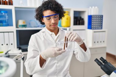 Laboratuvarda test tüpleri tutan bilim adamı üniforması giyen İspanyol bir genç.