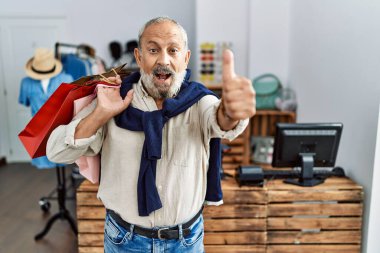 Butik dükkanında alışveriş torbaları tutan yakışıklı bir adam. Elle olumlu jest yapmayı onaylıyor. Gülümsüyor ve başarı için seviniyor. kazanan jest. 