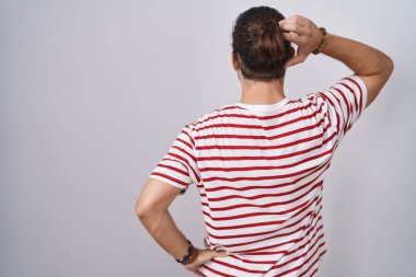 Hispanic man with long hair standing over isolated background backwards thinking about doubt with hand on head 
