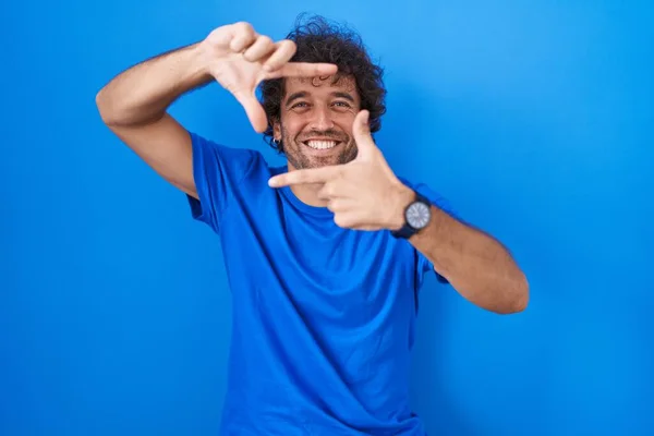 Jovem Hispânico Sobre Fundo Azul Sorrindo Fazendo Quadro Com Mãos — Fotografia de Stock