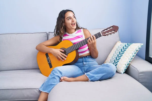 stock image Young beautiful hispanic woman playing classical guitar sitting on sofa at home