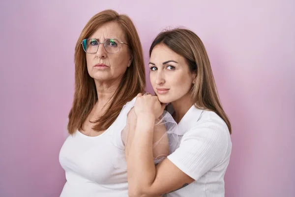 Hispanic mother and daughter wearing casual white t shirt relaxed with serious expression on face. simple and natural looking at the camera.