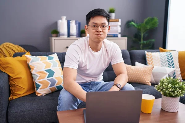 Young Asian Man Using Laptop Home Sitting Sofa Puffing Cheeks — Zdjęcie stockowe