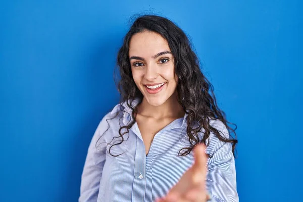 年轻的黑发女子站在蓝色的背景上 友好地微笑 握手致意和欢迎 成功的商业 — 图库照片