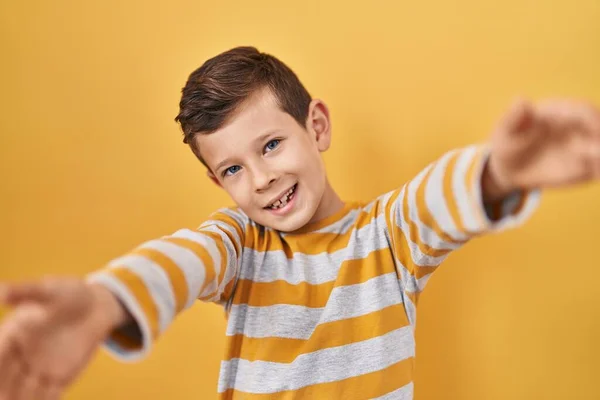 年轻的高加索小孩站在黄色的背景上 看着镜头 张开双臂拥抱 欢快的表达拥抱幸福 — 图库照片