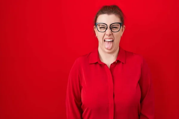 Mladá Hispánka Rudými Vlasy Stojící Nad Červeným Pozadím Vystrkující Jazyk — Stock fotografie