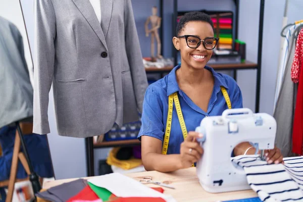 African american woman tailor smiling confident using sewing machine at tailor shop