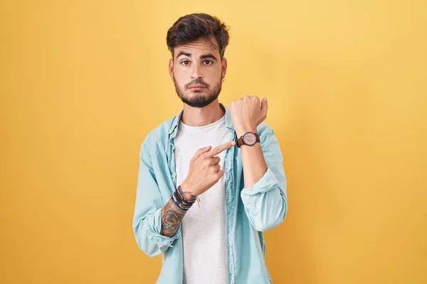 Young Hispanic Man Tattoos Standing Yellow Background Hurry Pointing Watch — Stock fotografie