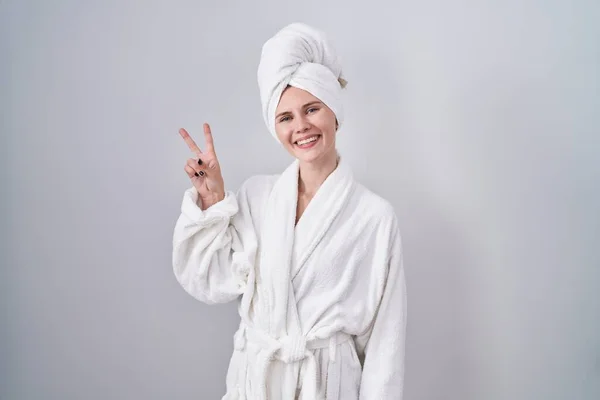 金发女人穿着浴衣 面带微笑地看着摄像机 手指在做胜利的标志 第二点 — 图库照片
