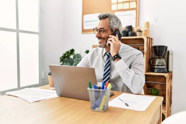 オフィスでスマートフォンで話すノートパソコンを使用している中年の白髪のビジネスマン — ストック写真