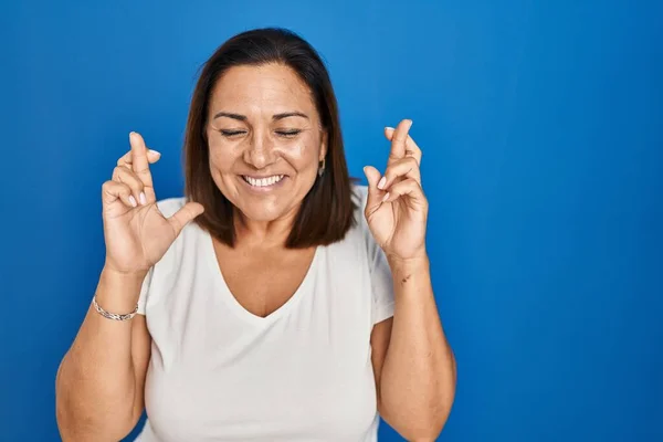 Hispanic Mogen Kvinna Stående Över Blå Bakgrund Gestikulerande Finger Korsade — Stockfoto