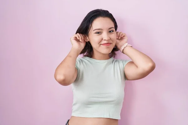 Hispanic Young Woman Standing Pink Background Smiling Pulling Ears Fingers — Φωτογραφία Αρχείου