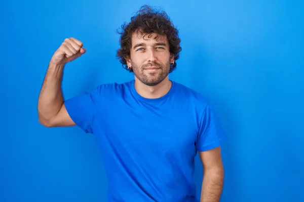 Jovem Hispânico Sobre Fundo Azul Pessoa Forte Mostrando Músculo Braço — Fotografia de Stock