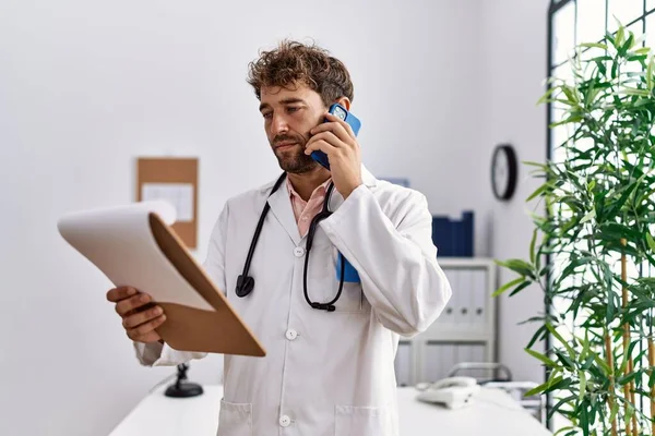 Young Hispanic Man Wearing Doctor Uniform Reading Diagnosis Talking Smartphone — Stock Photo, Image