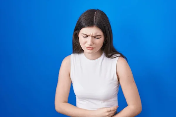 Stock image Young caucasian woman standing over blue background with hand on stomach because indigestion, painful illness feeling unwell. ache concept. 