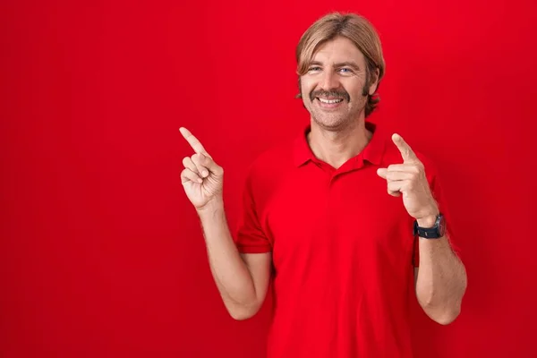口ひげを持つ白人男立ち上がっ赤の背景笑顔と見てカメラを指して2本の手と指で側面 — ストック写真