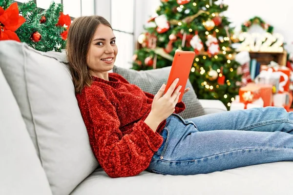 年轻的惊慌失措的女孩用触摸板坐在家里的圣诞树旁的沙发上 — 图库照片