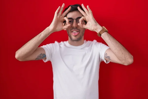 Young Hispanic Man Standing Red Background Doing Gesture Binoculars Sticking — Stok fotoğraf