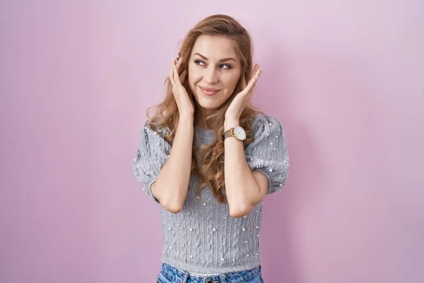 大きな音楽のノイズのためにいらいらする表情で指で耳を覆うピンクの背景に立つ美しいブロンドの女性 聴覚障害の概念 — ストック写真