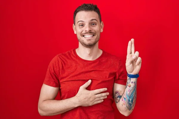 Kırmızı Arka Planda Duran Genç Spanyol Adam Gülümsüyor Elleri Göğsünde — Stok fotoğraf