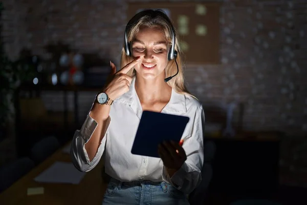 Young blonde woman working at the office at night pointing with hand finger to face and nose, smiling cheerful. beauty concept