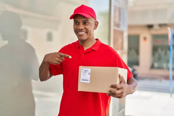 Young latin man delivery worker pointing with finger to package at street