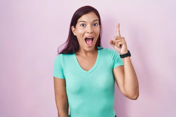 ピンクの背景に立っている若いヒスパニック系の女性は 成功したアイデアで指を指しています 興奮して幸せよ 第1位 — ストック写真
