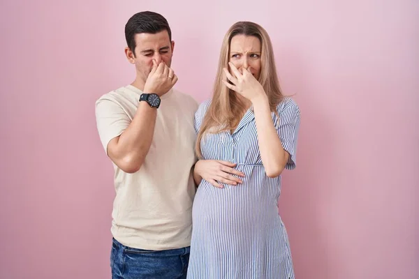 Young Couple Expecting Baby Standing Pink Background Smelling Something Stinky — Stock Photo, Image