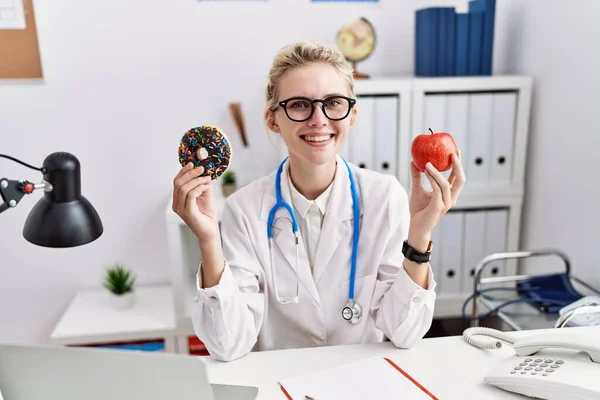 Młoda Lekarka Trzymająca Czerwone Jabłko Pączka Klinice Uśmiechająca Się Uśmiechem — Zdjęcie stockowe