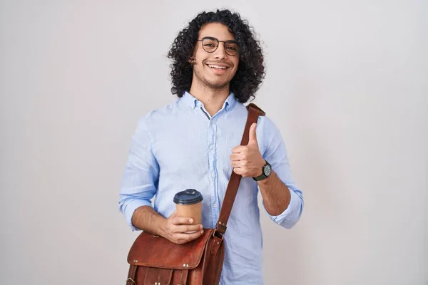 一个留着卷发的西班牙男人 一边喝着一杯咖啡 一边用手拿着快乐的大拇指做手势 赞成的表情看着相机显示的成功 — 图库照片