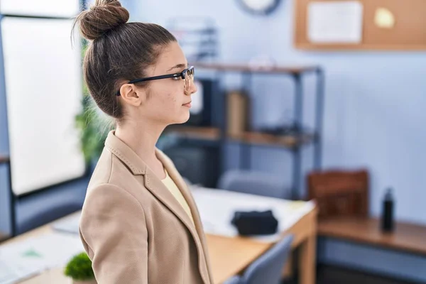 Teenager girl working at the office wearing glasses looking to side, relax profile pose with natural face with confident smile.